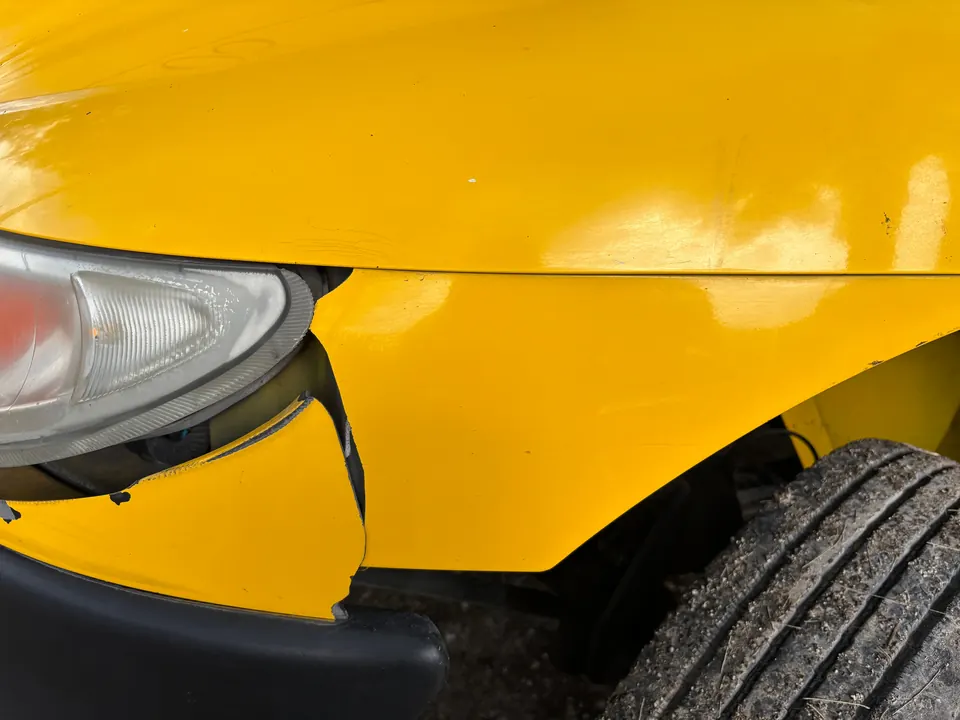 Beschadigd voorspatbord en koplamp van een gele auto, van dichtbij gefotografeerd