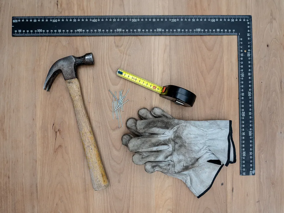 Hamer, winkelhaak, rolmaat, spijkers en werkhandschoenen op een houten tafel