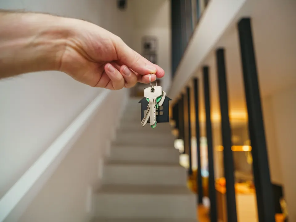 Hand die een sleutelbos met huisvormig label omhooghoudt in een woning met trap
